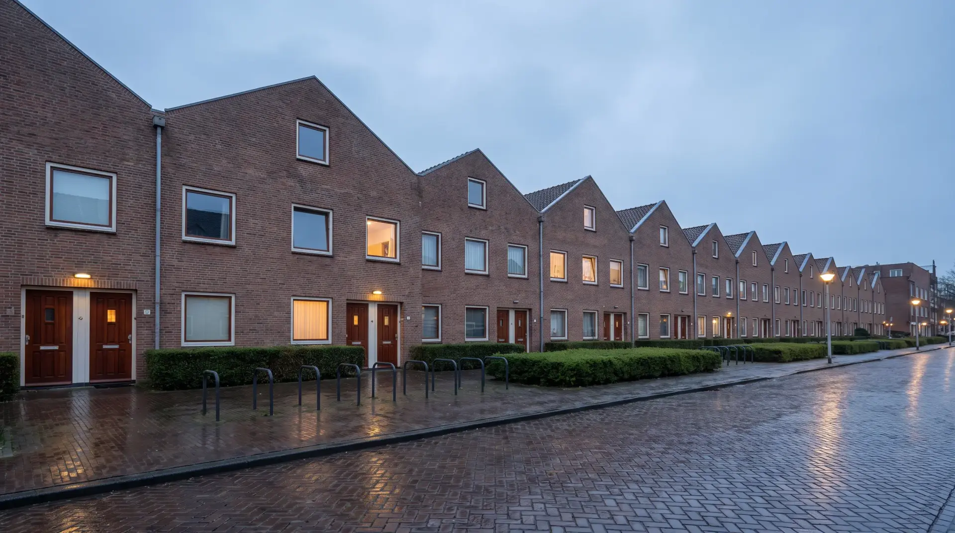Rij identieke Nederlandse huurappartementen met verlichte ramen in de avondschemering