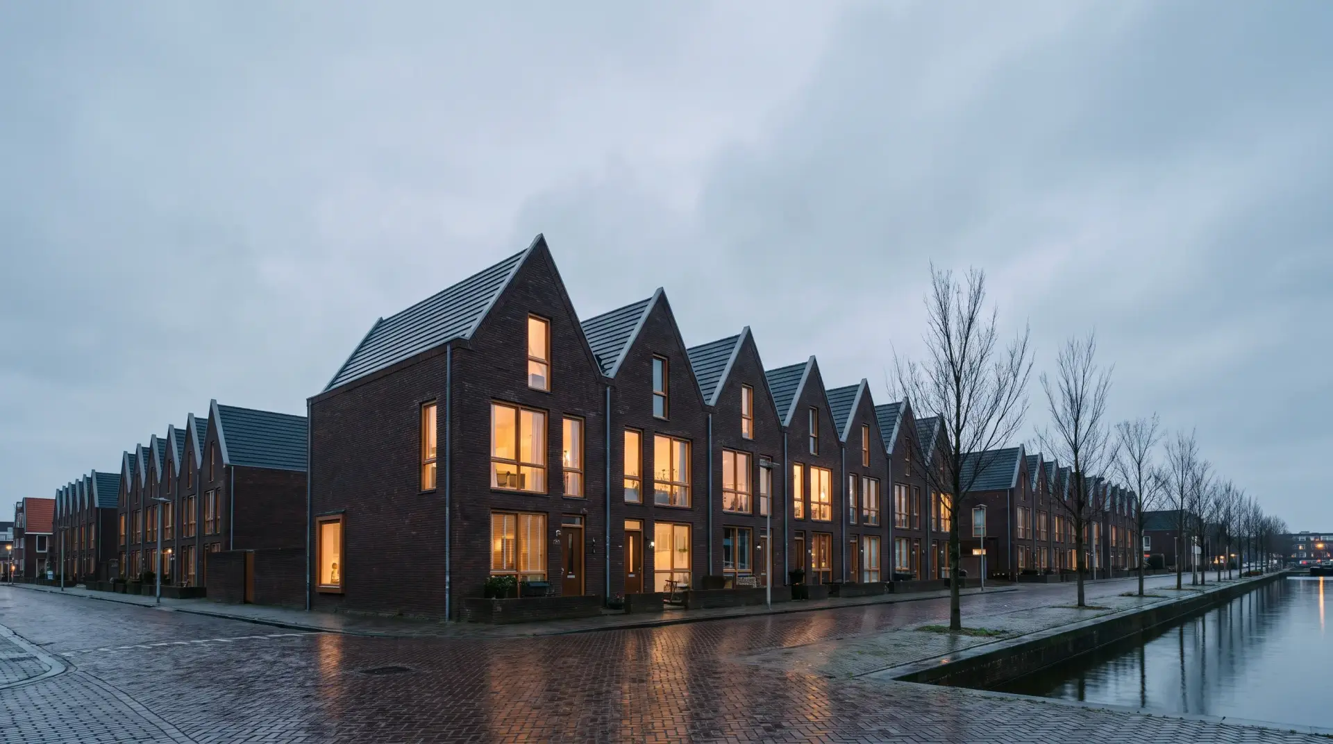 Rij Nederlandse bakstenen woningen met puntgevels langs een gracht in de avondschemering