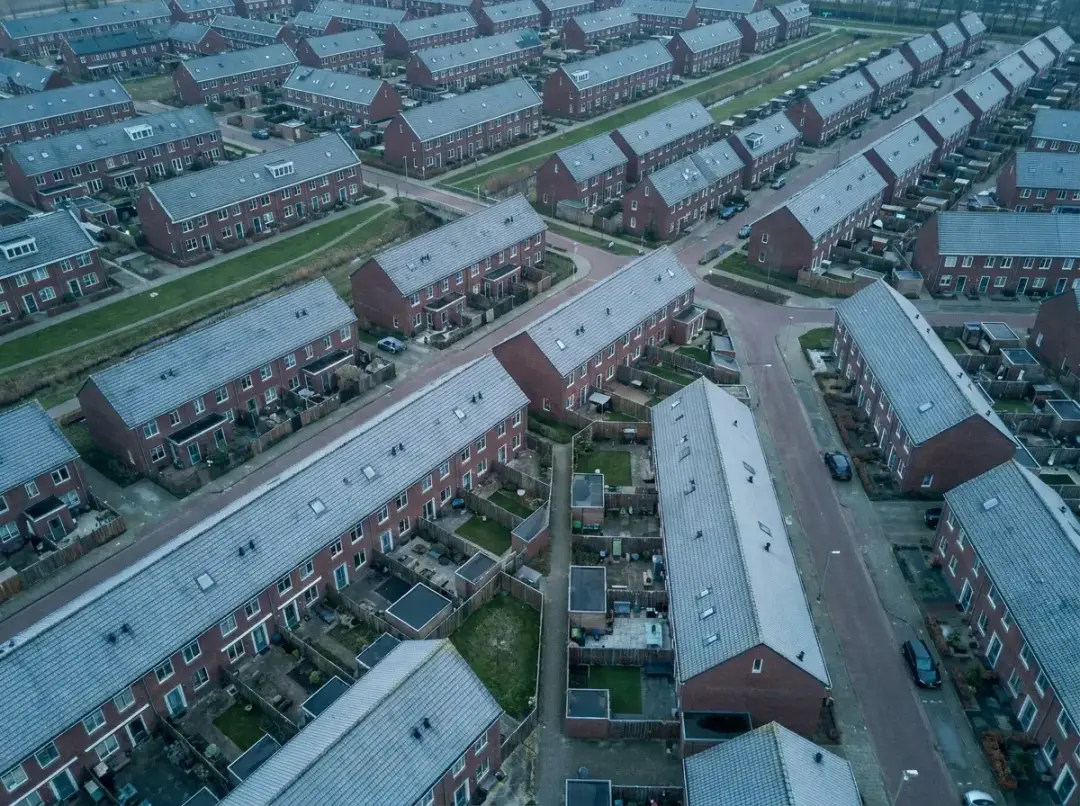 Luchtfoto van rijen identieke Nederlandse huurwoningen met achtertuinen